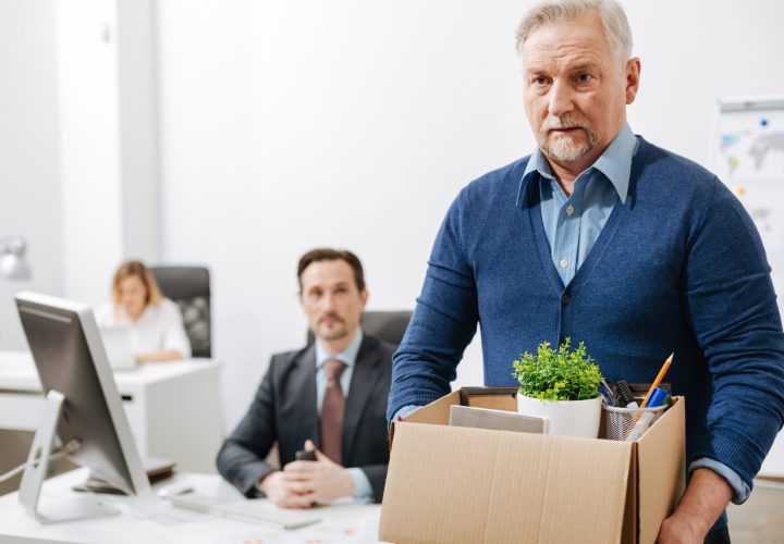 Frustrated elderly employee leaving office with box full of belongings